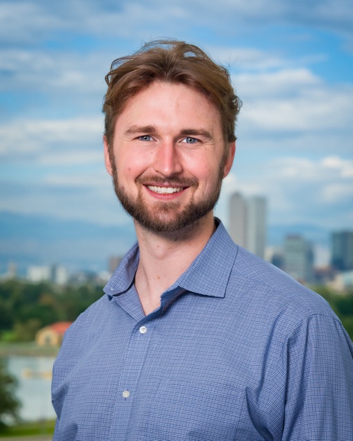 A portrait of David DeBonis (a.k.a David J DeBonis) in a blue shirt with the Denver Skyline and the Rocky Mountain front range in the background.